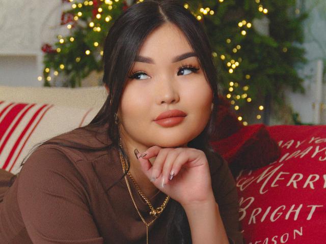 TeyaFaber has long dark hair, brown eyes, and full lips, wearing a brown top, with a gold chain necklace, resting her chin on her hand, looking to the side.