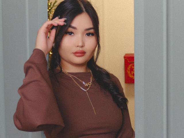 TeyaFaber with long black hair, brown long-sleeve shirt, gold chain necklace, and subtle makeup, standing in doorway, hand in hair, looking at camera, sexy, attractive, full lips.