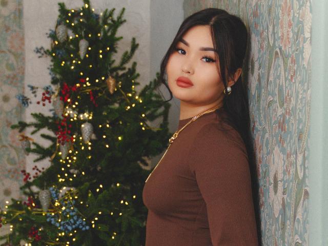 TeyaFaber with long black hair, brown dress, gold necklace, standing by a Christmas tree with lights and decorations, looking at the camera, sexy, cute, full lips, small ass.