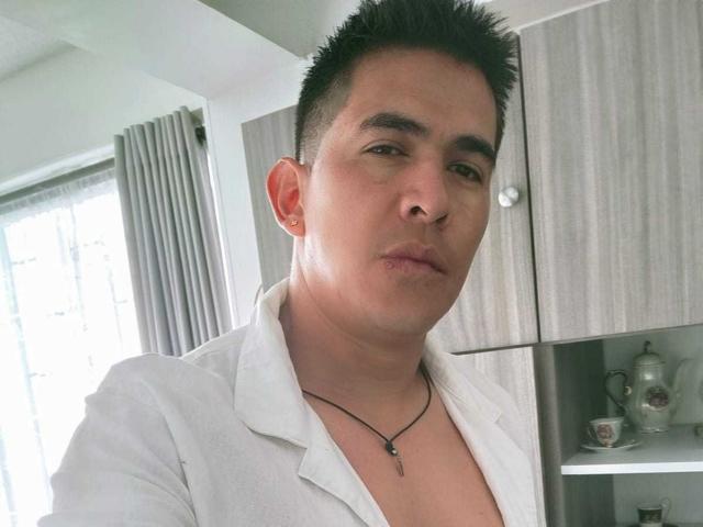 CaballeroDeLaNoches has short black spiky hair, a white shirt, and a necklace with a small pendant, looking at the camera with a neutral expression.