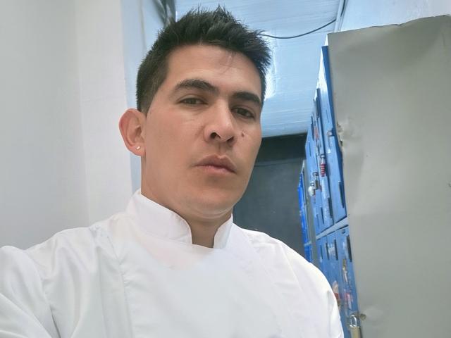 CaballeroDeLaNoches, a short-haired dude with dark eyebrows and a nose piercing, wearing a white chef's coat, looking serious in a kitchen.
