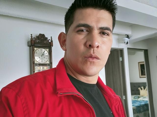 CaballeroDeLaNoches has a chubby face, dark short hair, and is pouting with his lips slightly pursed. He's wearing a red jacket over a black shirt.