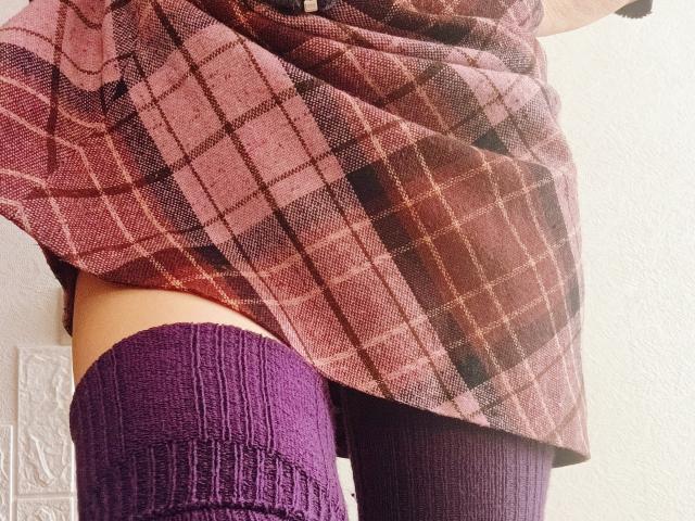 De roze geruite rok van MartLor wordt opgetrokken, waardoor haar paarse gebreide hoge sokken en haar blote billen zichtbaar worden. Haar rok heeft een geruit patroon, wat contrasteert met haar huid en de kousen..