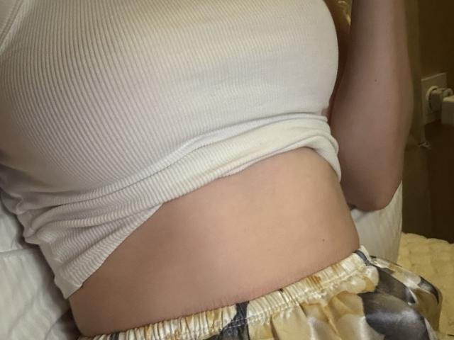 SelinaRose's white ribbed tank top is pulled up, exposing her small, bare belly and a hint of her soft, pale skin. She's wearing yellow and black patterned pants.