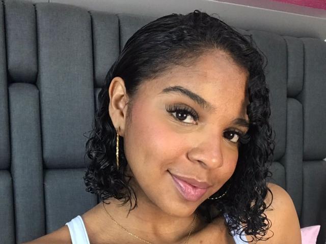 LisaMendez has curly black hair, brown eyes, and is sticking her tongue out. She's wearing gold hoop earrings and a light blue top, with a subtle smile.