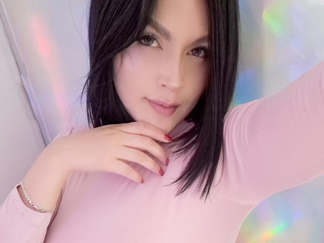 LinaStars has pale skin, black shoulder-length hair, brown eyes, pink top, red nail polish, and a silver bracelet, with a subtle smile, hand near chin.