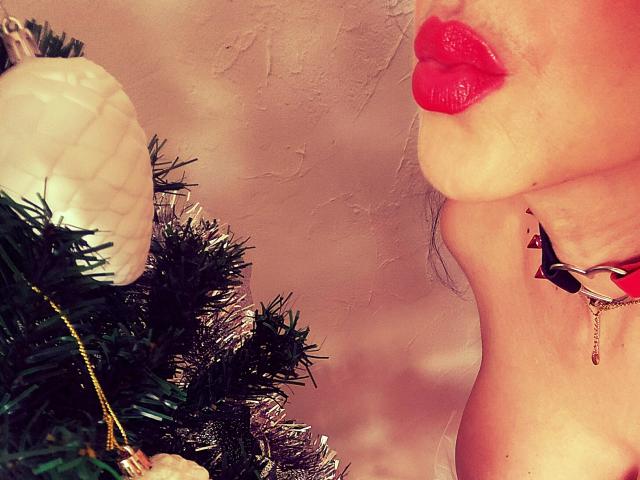 De rode lippen en de neusring van LaParisienne staan naast een kerstboom met witte versieringen en groene takken. Ze draagt een zwarte choker met een klein hangertje..