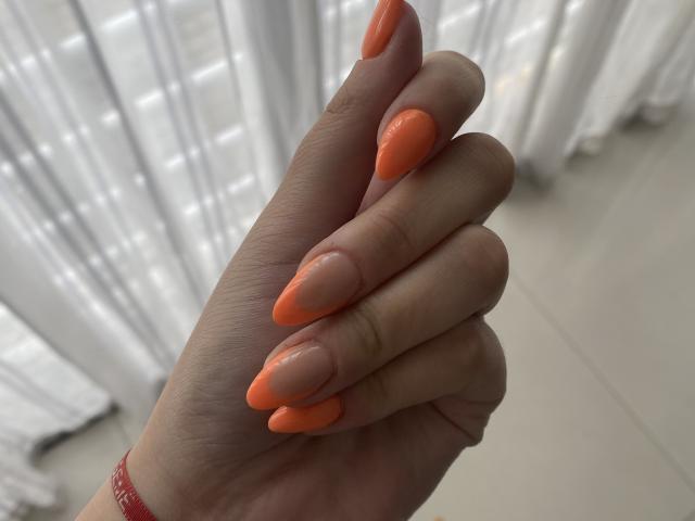 AlexaLip's hand with long, shiny, orange-tipped, nude-colored nails, lightly touching her fingers. She's wearing a red wristband.