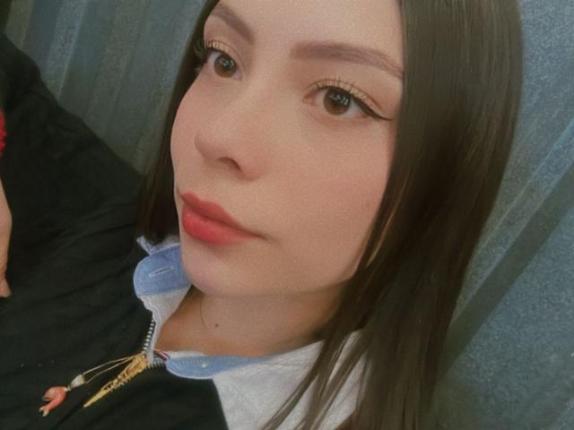 FrancesscaMoretty with long brown hair, light skin, and pink lipstick, wearing a blue collared shirt under a black jacket, showing her face and subtle eyeliner.
