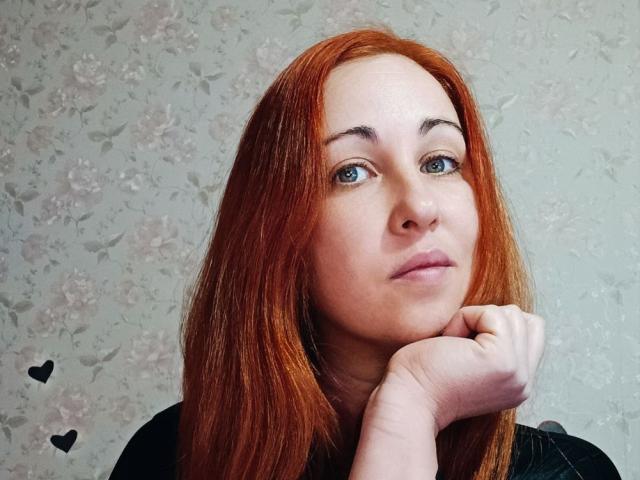 JillSilvies has red hair, blue eyes, and fair skin. She rests her chin on her hand with a slightly annoyed expression. Two black hearts are on the left.