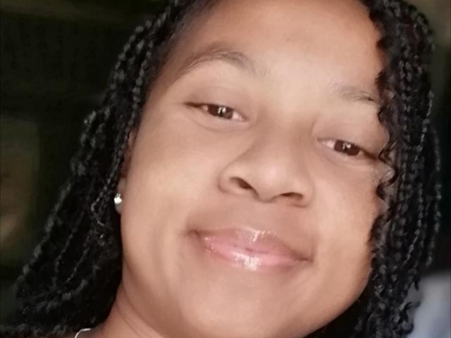Edrwina69's face with shiny pink lips, slight smile, dark brown eyes, and black braided hair. She's wearing a small diamond earring on the left side of her face.