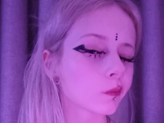 ExcitedBlizzard has pale skin, long blonde hair, black eyeliner with star accents, nose ring, and lower lip piercing, all under purple lighting.