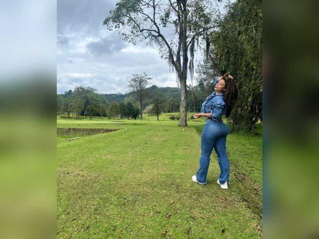 CourtneyLow in a blue, tight, long-sleeve, and pant combo, showing off her curvy ass and small, perky tits, standing on grass with trees in the background.