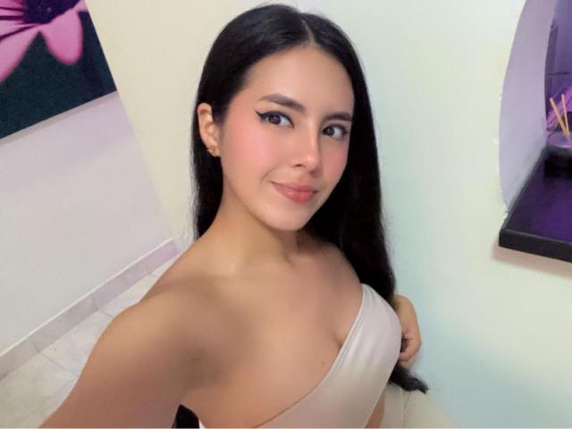 EimmyPark with long black hair, light skin, and a smile, wearing a beige off-shoulder top, showing her small tits and bare shoulder in a selfie.