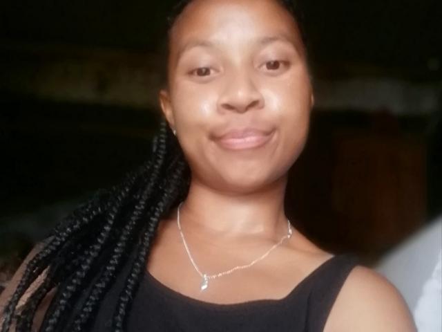 Edrwina69 has smooth brown skin, black braided hair, and a subtle smile. She's wearing a black sleeveless top and a silver necklace with a small pendant.