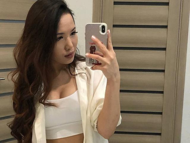 MishelBlessing with wavy brown hair, wearing a white crop top and open shirt, taking a mirror selfie, showing her small tits, holding a phone with a red sticker.