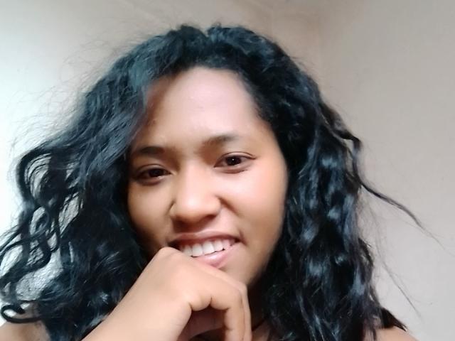 LoveHer has curly black hair, brown eyes, and a cute smile, with her finger resting on her chin, showing off her small, cute teeth and soft, brown skin.