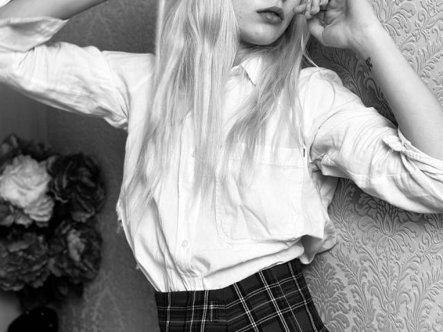 Lialit with long blonde hair, wearing a white shirt and plaid skirt, hand in hair, black and white photo, visible tattoo on wrist, subtle lipstick.