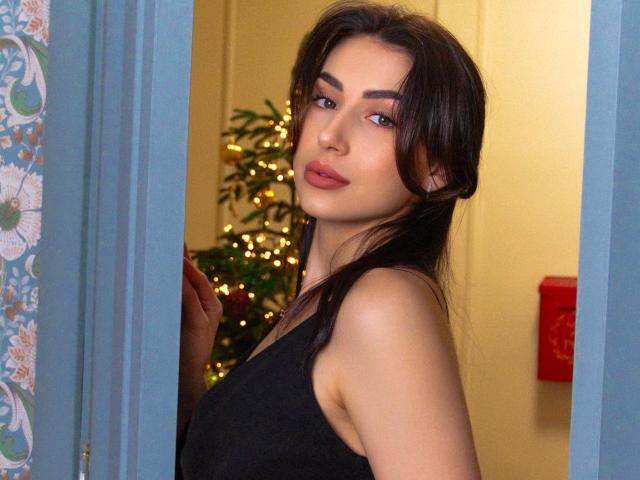 OliviaCluff with dark brown hair, medium tits, wearing a black tank top, standing in a blue doorway, looking over shoulder, soft smile, subtle makeup, Christmas tree in background.