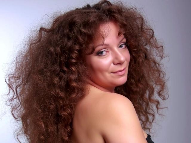 Delight-Alice has curly brown hair, light skin, and is looking over her shoulder with a slight smile. She's topless, showing her bare back and small, perky tits.