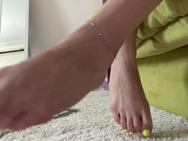 AlicePrings' bare foot with neon yellow toenails, a silver ankle bracelet, and a slightly red heel resting on a fluffy carpet.