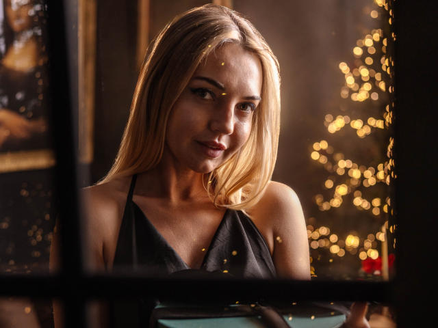 LettieSweet with blonde hair, wearing a black halter top, has a cute smile, soft light, bokeh, and a warm, inviting look. Her tits are slightly visible, looking sexy.