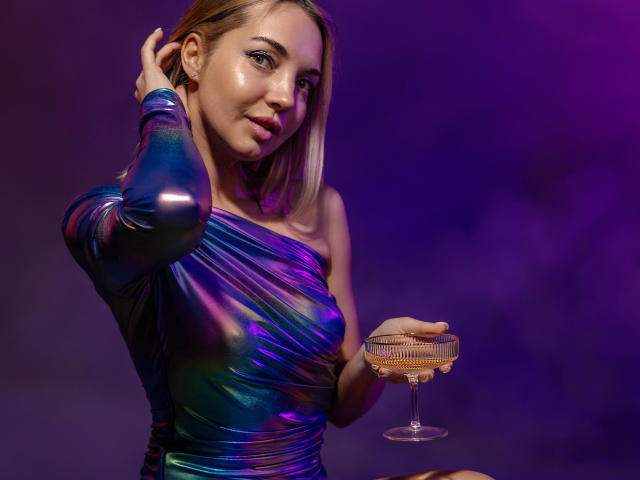 LettieSweet with shiny purple-blue metallic dress, holding a glass of wine, right hand in hair, purple and blue lighting, short blonde hair, slight smile, visible breast.