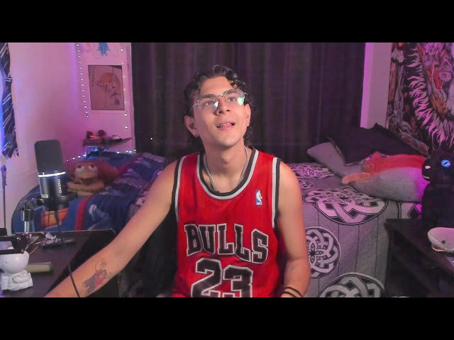 AntonyGaldro, wearing a red Bulls jersey with number 23, has glasses, a necklace, and a tattoo on his right forearm, sitting in a dimly lit room.