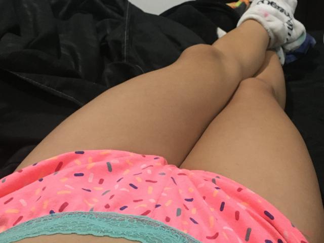 LaraHottie's pink, sprinkle-patterned booty shorts, showing her brown thighs, crossed at the ankles with white socks, lying on a black blanket.