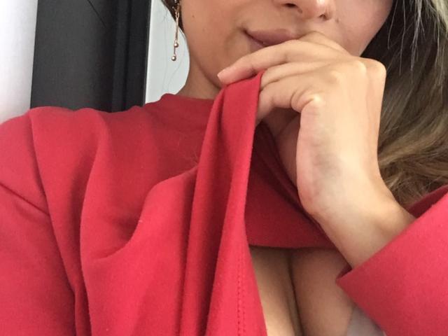 LaraHottie with her hand covering her mouth, wearing a red dress, exposing her tits, her pink nipples barely visible, brown hair, earrings, and a subtle smile.