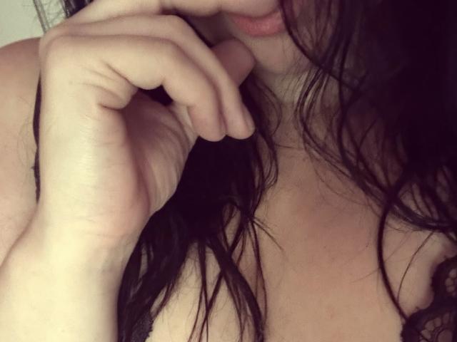 SunshineSofia's hand touches her slightly parted lips, with wet, dark hair covering her large, bare tits. Her fingers gently hold her chin, showing soft, pink lips.