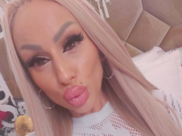 HotBebe69x mit sinnlichen, rosafarbenen Lippen, langen blonden Haaren, viel Make-up und großen Reifenohrringen, sieht auf dem Selfie sexy und verführerisch aus. Die Brüste sind nicht sichtbar..