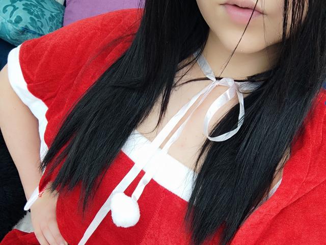 Kkatalina's red, fluffy dress with white pom-poms and ribbons, showing her cleavage and black hair, has her hand on her hip, with her lips slightly parted.