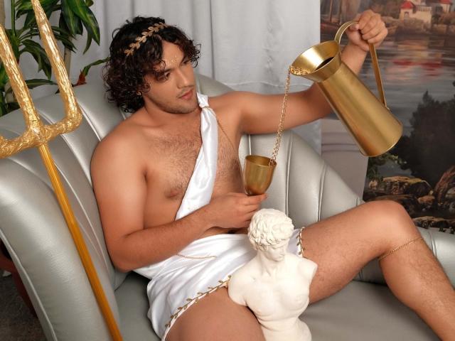 FreyrStyle69 with curly brown hair, wearing a white toga, pours gold water from a gold pitcher onto his chest, sitting on a silver chair, with a white statue nearby.