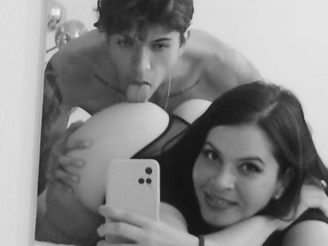 HottersTeam with dark hair and HottersTeam with curly hair, both naked, HottersTeam's tongue on HottersTeam's butt, HottersTeam taking selfie with phone in mirror.