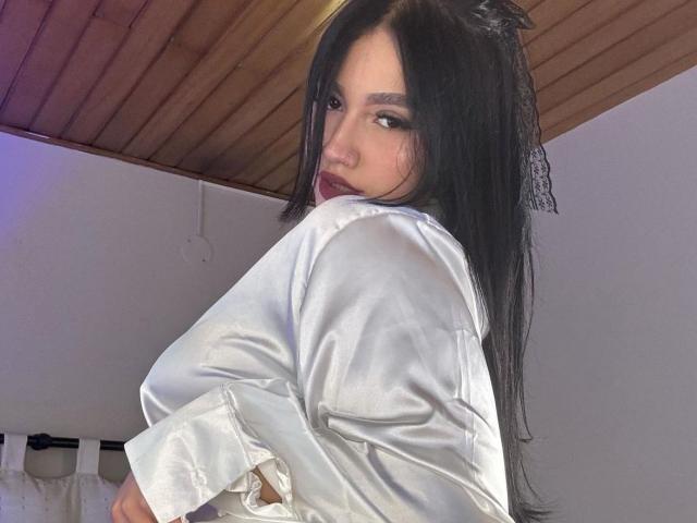 HiilaryFox with long black hair, wearing a shiny white satin shirt, looking over her shoulder with a slight pout, wooden ceiling, and soft purple lighting.
