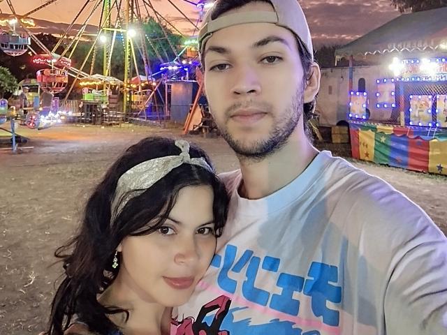 Two HottersTeam, a dude with a beard in a backwards cap and a chick with a headband and earrings, standing at a carnival, both smiling at the camera.