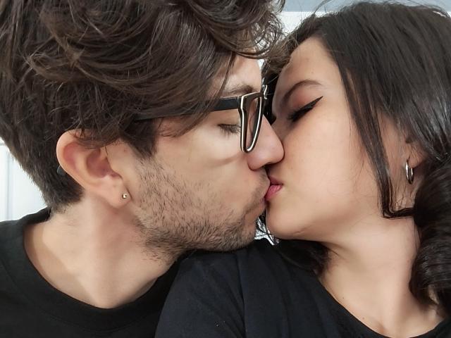 HottersTeam with messy brown hair and glasses, kissing HottersTeam with dark wavy hair and hoop earrings, both wearing black shirts, tongues touching, eyes closed.