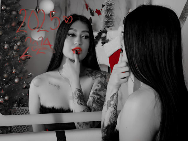 EmmaRosseti with tattoos, long dark hair, red lipstick, finger in mouth, mirror reflection, Christmas tree, white stockings, black fur strap, looking seductive, bare breasts visible.