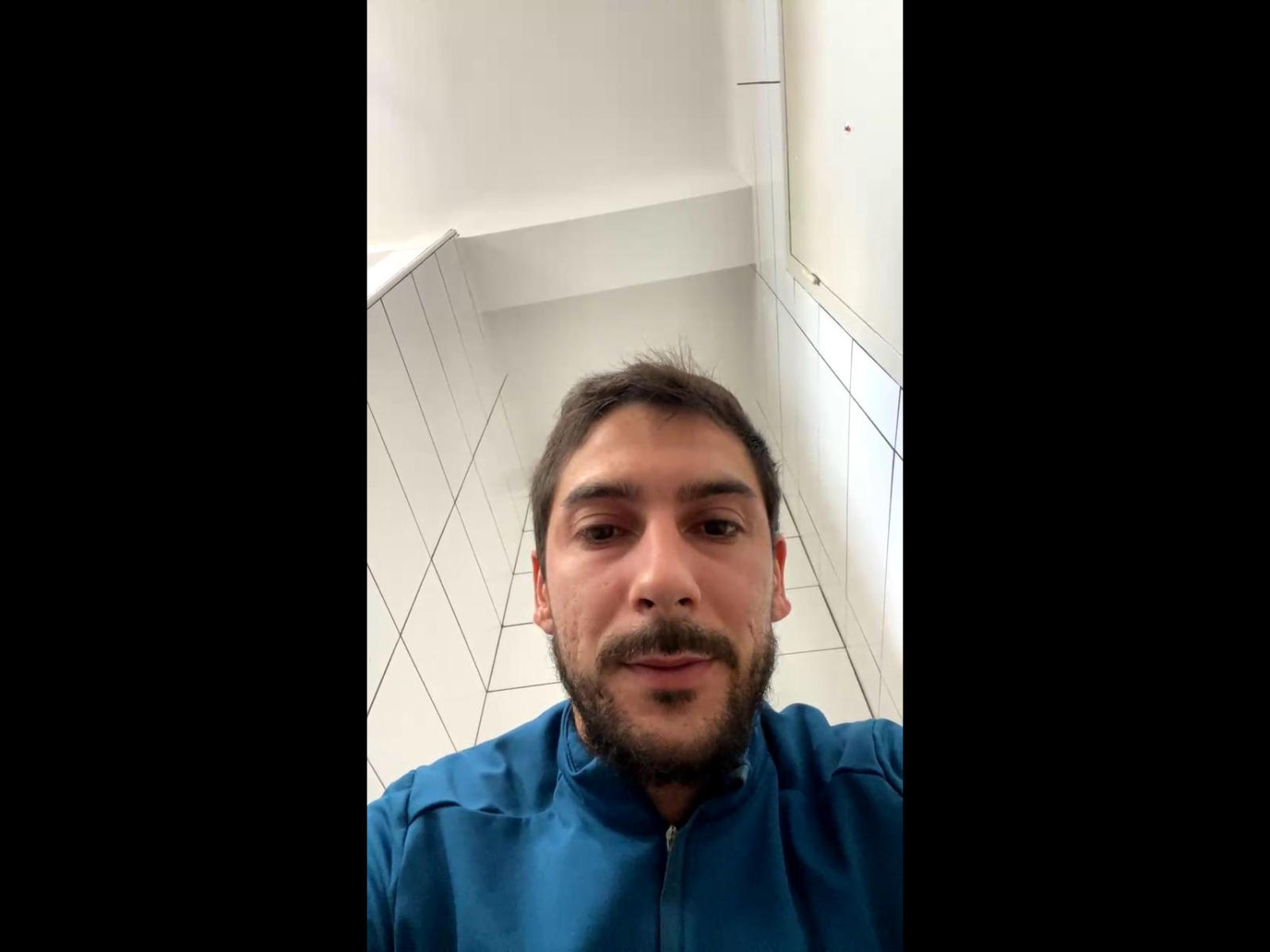 BichoSun, a bearded guy with brown hair and a blue zip-up shirt, stares at the camera in a white-tiled bathroom. His ass is not visible.