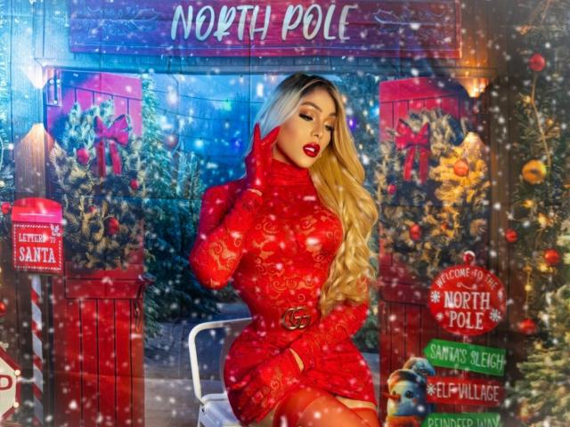 LorentsTS with long blonde hair, red lace dress, and belt, showing off her curvy ass and big tits, wearing red gloves, in a snowy Christmas-themed photo.