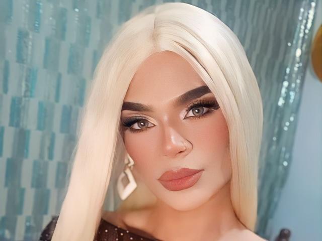 Artemisa Taylor ha i capelli biondo platino, sopracciglia folte, un pesante eyeliner nero, ciglia lunghe e rossetto nude. Indossa una maglietta marrone con orecchini di diamanti e un anello al naso..