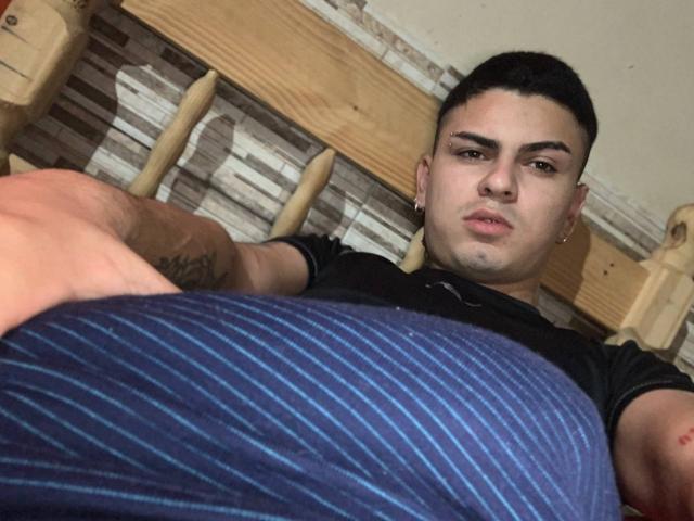 SarethOky, un ragazzo latino con i capelli neri corti, che indossa una maglietta nera, ha un'espressione seria e giace supino con un cuscino a righe blu in primo piano..
