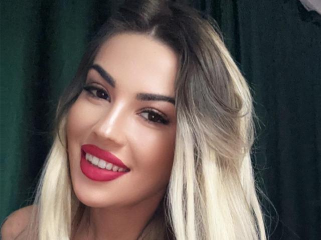 ZoeyMarie heeft blond haar met een ombre-effect, rode lippenstift en een sexy glimlach, met donkere wenkbrauwen en bruine ogen. Haar achterkant is niet zichtbaar, alleen haar gezicht..