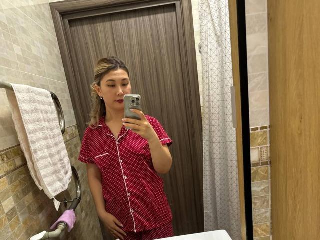 SoftGeraldine in rode pyjama met stippen, met een telefoon in haar hand, die een spiegel-selfie maakt, staand in een badkamer, met haar hand op haar achterwerk, lichtbruin haar, rode lippenstift, neutrale uitdrukking..