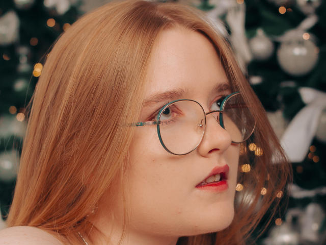 BonnieBell has red hair, round glasses, and red lips, with a slight open-mouth expression. She's looking to the right, showing fair skin and a subtle nose. Boobs are not visible.