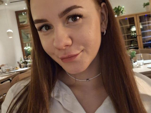 InfiniteDesire with brown hair, subtle smile, light skin, small nose, brown eyes, white shirt, silver necklace, small earrings, slightly pouty lips, in a dimly lit restaurant.