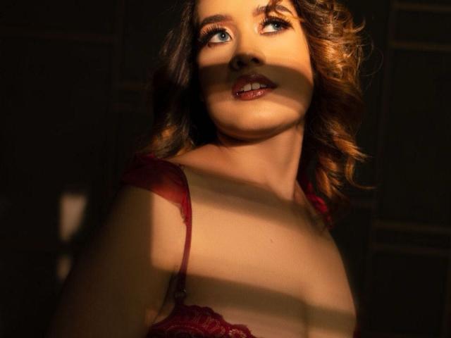 AkiraZanoli with curly brown hair, red lace bra, and sunlit face, looking up with wide eyes and slightly parted red lips, shadow across chest, light from left.