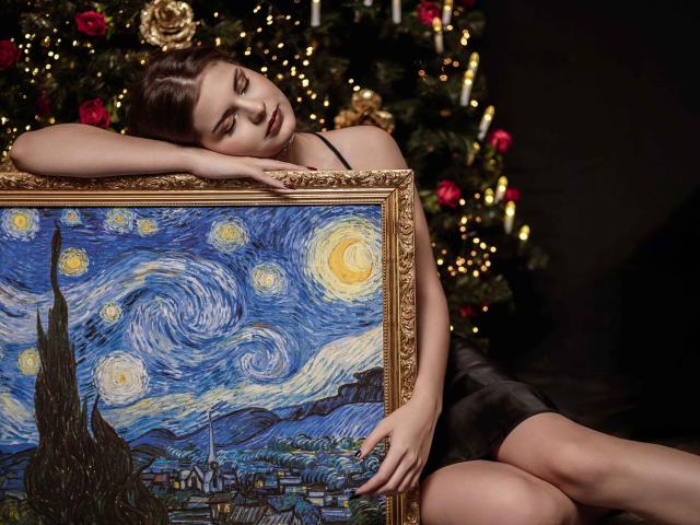 AdeliaLove leans on a Van Gogh painting, eyes half-closed, wearing a black dress, with her tits barely visible, against a Christmas tree with candles and red roses.