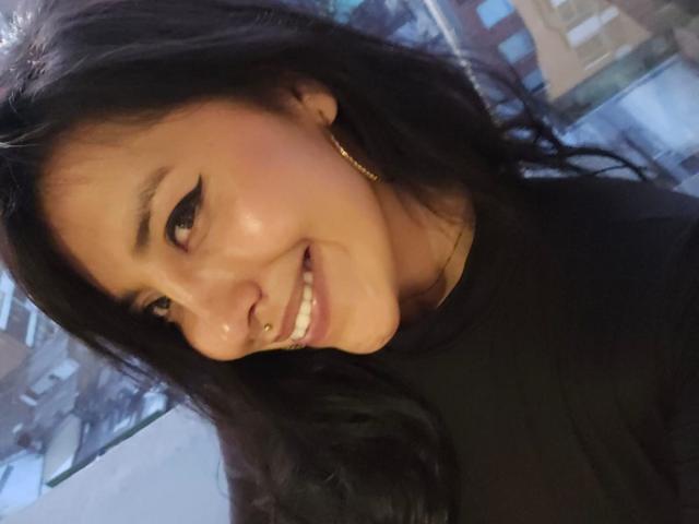 ElizabethMacy has dark hair, a nose ring, and a black top, smiling with eyeliner and gold earrings, showing her teeth in a selfie. Her ass is not visible.